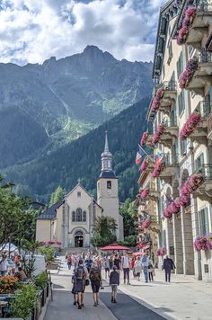 people are walking down the street in front of buildings with mountains in the back ground