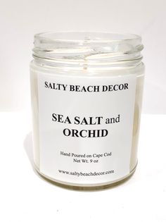 sea salt and orchid scented candle in a glass jar on a white surface with the words salty beach decor