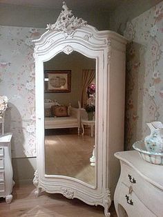 a white dresser sitting next to a mirror on top of a wooden floor covered in furniture