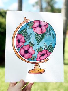 a hand holding up a card with flowers on it and a globe in the background