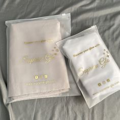 two white sheets with gold lettering on them are laying on a gray bed sheet that says supreme glo