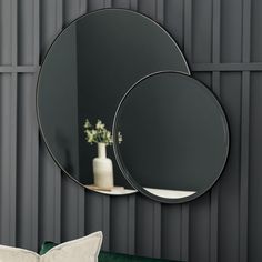 two round mirrors hanging on the wall next to a green couch and vase with flowers