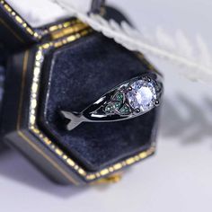 an engagement ring sitting on top of a blue velvet box next to a white feather