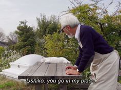 an old man standing at a picnic table with his hand on the ground next to him