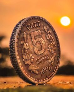 a five rupees coin sitting on top of a field with the sun in the background