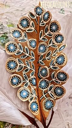 a wooden brooch with blue and white designs on it's side, sitting on top of a leaf