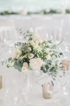 a vase filled with white flowers sitting on top of a table next to wine glasses