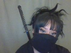 a woman wearing a black mask and holding a knife in front of her face with hair blowing back