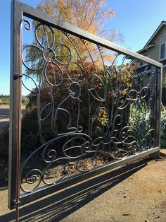 a large metal gate sitting in front of a house next to a tree and bushes