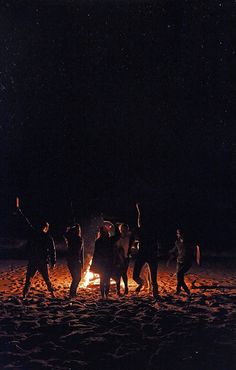 a group of people standing around a campfire at night with their arms in the air