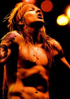 a shirtless man with long hair and tattoos on his chest standing in front of lights