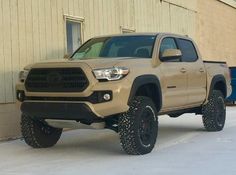 a tan toyota truck parked in front of a building with snow on the ground next to it