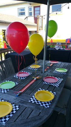 the table is set up with plates and balloons for an outdoor birthday party at home