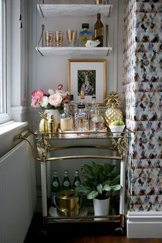 a bar cart in the corner of a room with flowers and bottles on top of it