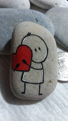 a rock with a drawing of a person holding a heart on it and two coins in the background