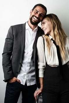 a man and woman standing next to each other in front of a white wall smiling