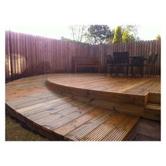 a wooden deck with chairs and table in the back yard, next to a fence