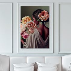 a white couch sitting next to two framed pictures on the wall with flowers in front of it