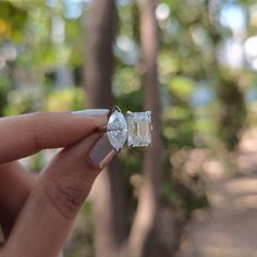 a woman's hand holding an engagement ring with two pear shaped diamonds