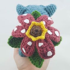 a hand is holding a crocheted flower with white dots and green leaves on it