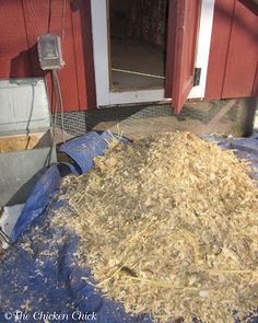 a pile of hay sitting on top of a blue tarp in front of a red building