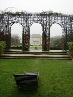 a bench sitting in the middle of a lush green park next to a large building