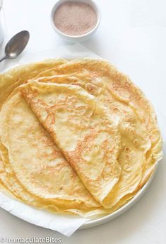 three quesadillas on a white plate next to two cups of coffee and spoons