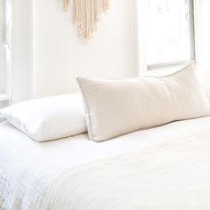 a bed with white sheets and pillows in front of a wall hanging on the wall