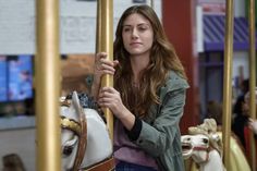 a woman standing next to a merry go round at an amusement park with her hand on the handle