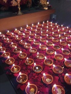 many candles are lit in small bowls on a table with red flowers and other decorations