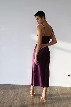 a woman in a purple dress standing on a wooden floor with her back to the camera