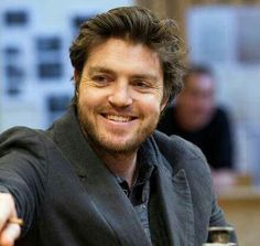 a man sitting at a table with a fork and knife in his hand, smiling