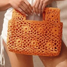 a crocheted orange purse being held by someone's hand with both hands