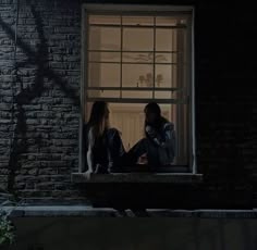 two people sitting on a window sill at night