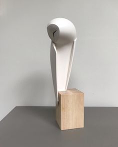 a white sculpture sitting on top of a wooden block in front of a gray wall