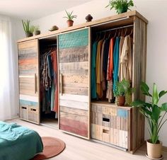 a room with a bed, plant and some clothes hanging on wooden cabinets in it