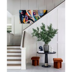 a painting hangs on the wall next to a table with two stools and a potted plant