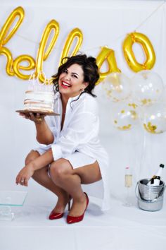 a woman holding a cake in front of balloons and the word hello spelled on it