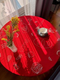 a red table topped with a vase filled with yellow flowers next to a white window