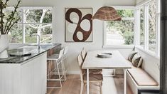 a kitchen with white walls and wooden flooring next to a dining table surrounded by chairs