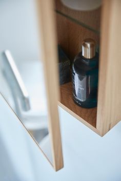 a bottle of cologne sitting on top of a wooden shelf next to a toilet paper dispenser