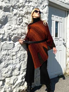 "Fall Knit Steampunk Ruffle Wrap | Boho Alpaca Black Orange Poncho, Wool Poncho Cape For Women This flirty, ruffled, alpaca wool blend hand-knitted wrap in black and burnt orange tons, is light and warm. It is a four-season piece and is ideal for layering.  The colour palette of this versatile shawl is definitely jeans friendly.  STYLE This dressy/casual piece is an excellent travel companion.  Works well with jeans, leggings, dress pants or over a solid dress adding a flowy elegance of a shawl. Endless in its versatility and fits most sizes make it a great gift idea. Material: Alpacas Wool Blend WAYS TO WEAR SEE FAQ's FOR WAYS TO WEAR AS A SHAWL, FITTED LOOK, BELTED LOOK AND SCARF. SIZING Length is approx. 30\" Fits sizes S- 3xl Please inquire about larger sizes Our model Elana is size 8 Acrylic Poncho Shawl For Fall, Acrylic Shawl Poncho For Fall, One Size Acrylic Poncho For Fall, Fall Knitted Poncho Cape, Knitted Fall Poncho Cape, Knitted Poncho Cape For Fall, Black Cape For Fall Festivals, Black Fall Festival Cape, Bohemian Knitted Poncho For Fall