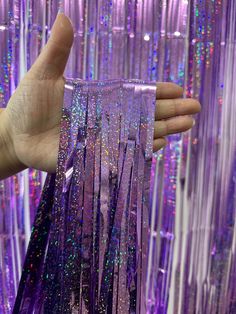 a hand holding up a purple curtain with multicolored sequins on it