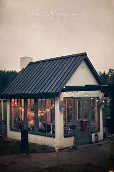 a small white house with lots of lights on it's windows and tin roof