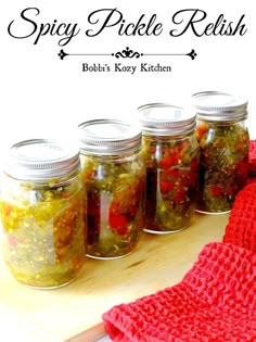 jars filled with pickle relish sitting on top of a wooden table next to a red towel