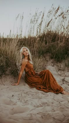 a woman sitting on top of a sandy beach next to tall grass and sea oats