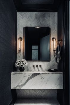 a bathroom with marble counter tops and black walls, along with two wall sconces