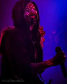 a man wearing a mask and holding a microphone in front of a purple lit background