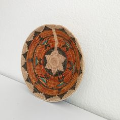 a woven basket hanging on the wall next to a white wall with a black and orange design