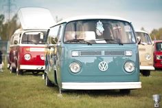 an old vw bus is parked in the grass with other vans behind it on display